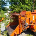 Orange wood chipper beside a pile of leafy cut branches